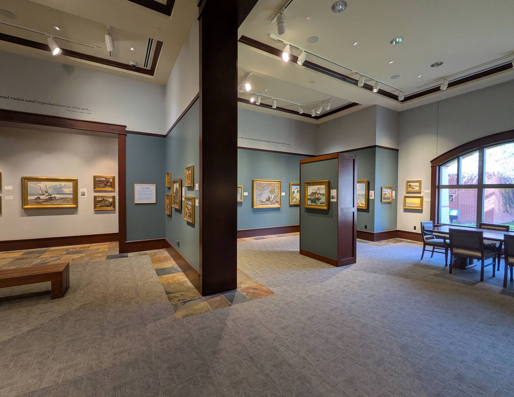 Photograph of the interior of a gallery with paintings hanging on the walls